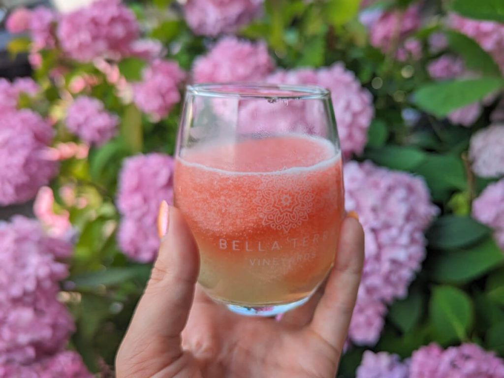 Frozen Pink and Green Beverage in Clear Wine Glass in Front of Pink Flowers